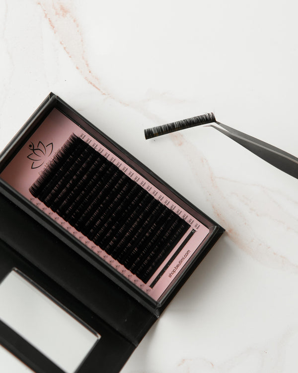 Beutimi FauxMink Lashes 0.02MM in black displayed in pink-lined tray with applicator tweezers on marble surface