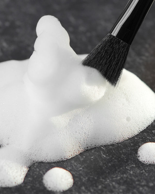 Beutimi Cleansing Brush with soft black bristles applying white lather foam on dark surface