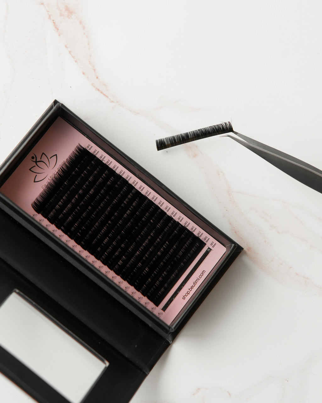 Beutimi FauxMink Lashes 0.02MM in black displayed in pink-lined tray with applicator tweezers on marble surface