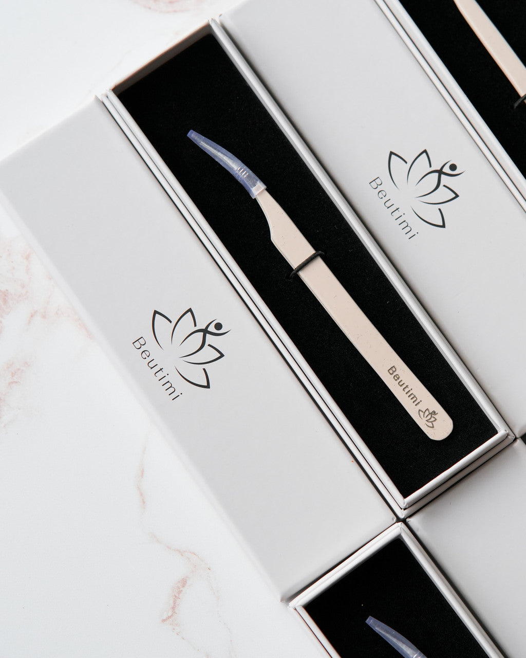 Beutimi Thrive Tweezer with cream handle and blue tip displayed in open white branded packaging on marble surface