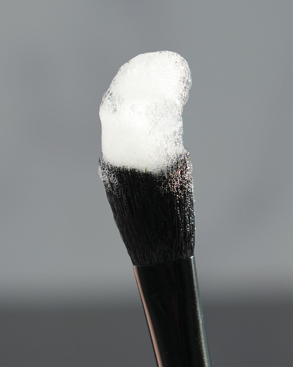 Beutimi Cleansing Brush with soft black bristles tipped in white powder against a gray background