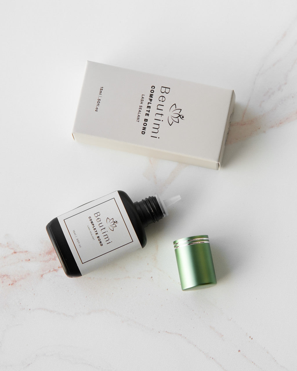 Beutimi Complete Bond lash sealer in dark glass dropper bottle with green cap, displayed with white packaging box on marble surface