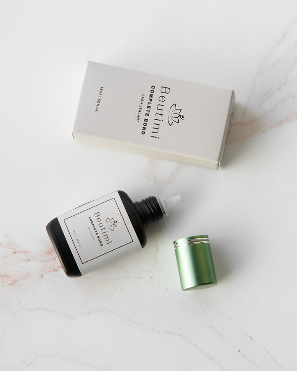 Beutimi Complete Bond lash sealer in dark glass dropper bottle with green cap, displayed with white packaging box on marble surface