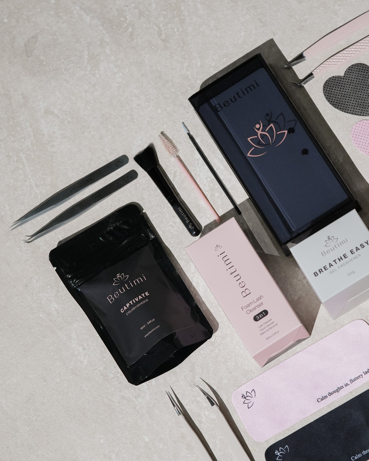 Beutimi Pro Kit laid out with black tweezers, pink foam lash pad, dark blue box, and training cards on white background