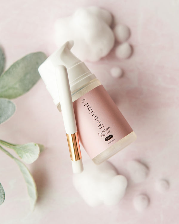Beutimi Foam Lash Cleanser bottle with white pump dispenser and gold accents displayed on pink background with eucalyptus leaves