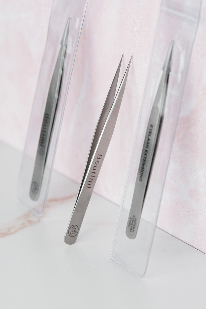 Beutimi Balance Tweezer displayed with two other tweezers in clear packaging against a pink and white background