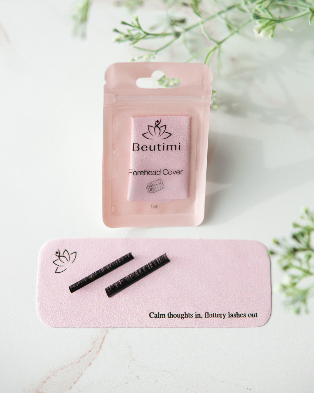 Beutimi Forehead Cover in pink packaging displayed with two black lash strip holders and motivational mat reading "Calm thoughts in, fluttery lashes out"