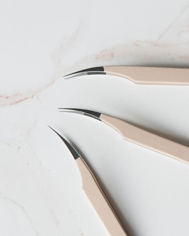 Three Beutimi Thrive Tweezers with beige handles and ultra-fine black tips arranged on white marble surface