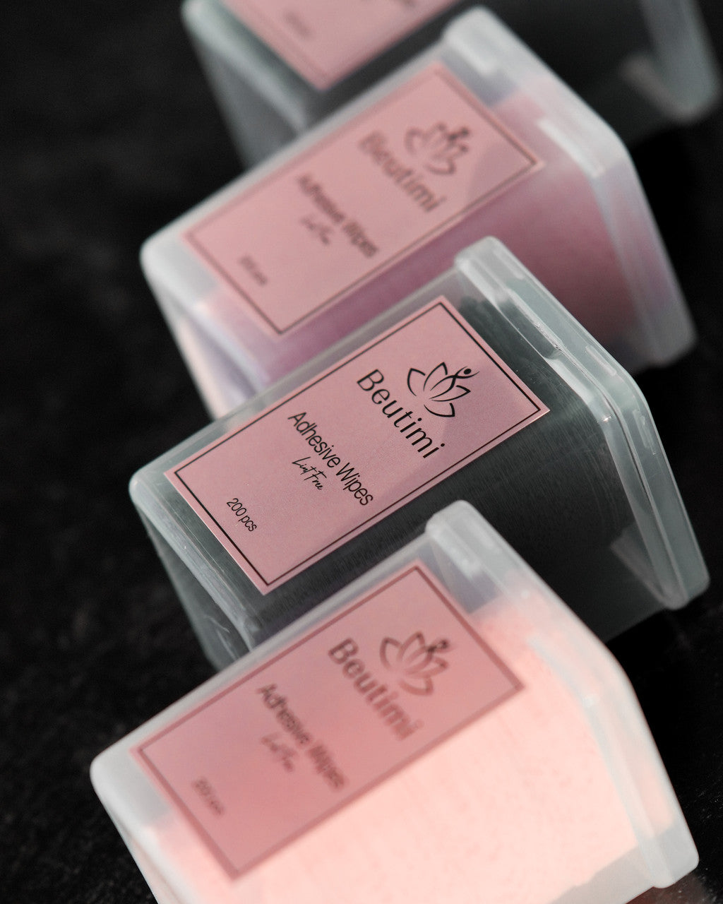 Beutimi Lint Free Adhesive Wipes in pink and black packaging arranged diagonally on dark background