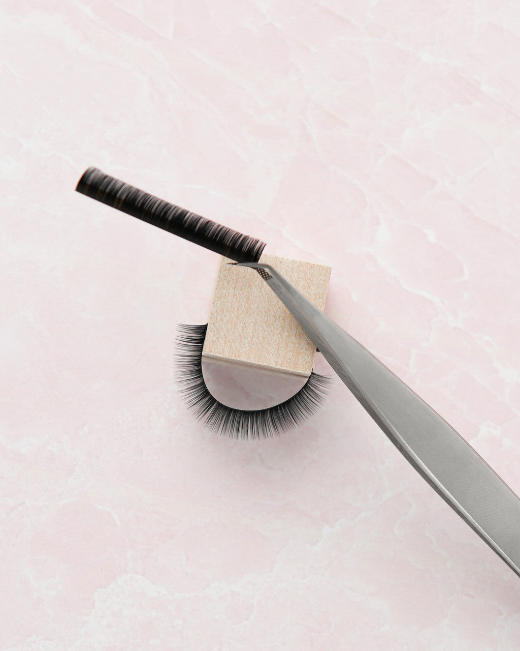 Beutimi FauxMink Lashes 0.05MM displayed on wooden block with silver tweezers and applicator brush against pink background