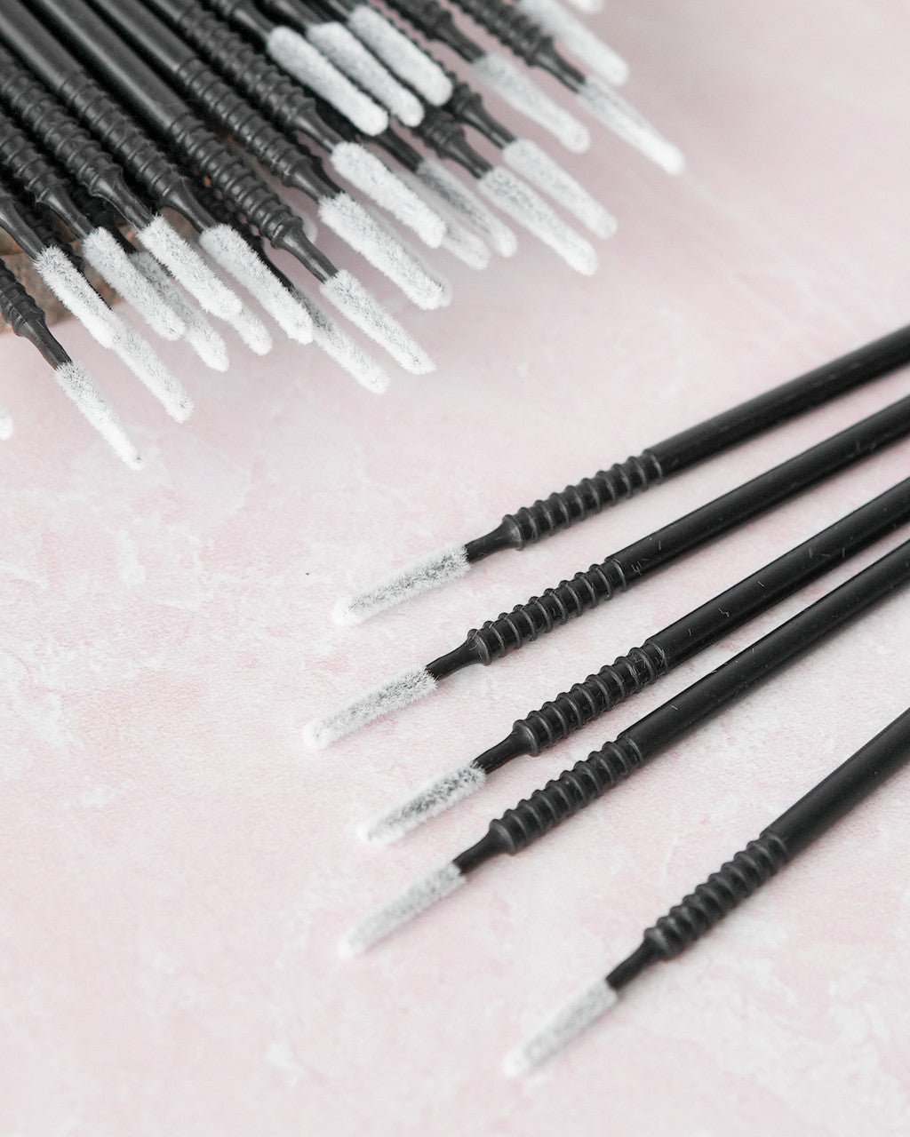 Beutimi Masterpiece Detailers micro brush applicators with black handles and white bristles arranged in rows on pink background