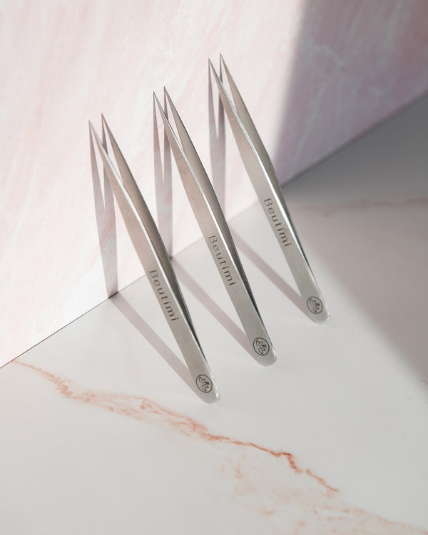 Three Beutimi Balance Tweezers with pointed tips arranged in a row on a white surface, casting shadows