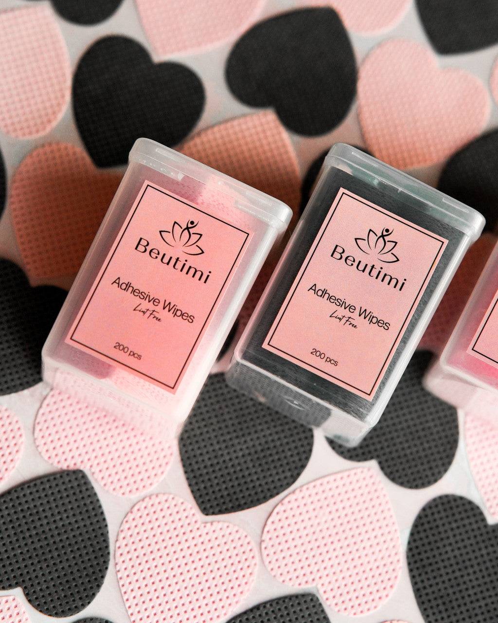 Two Beutimi Lint Free Adhesive Wipes packages in pink and black sit on a heart-patterned background