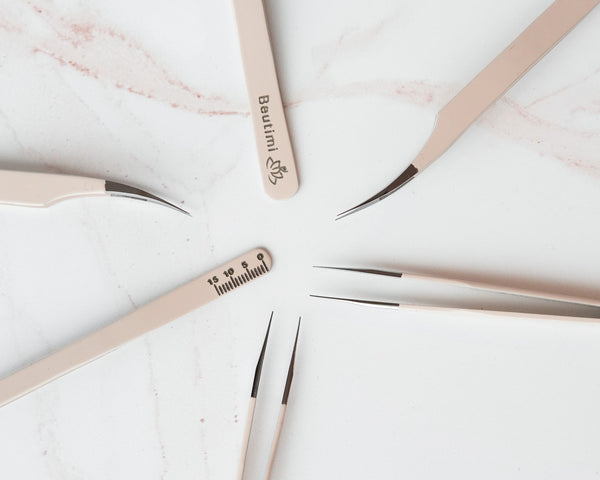 Beutimi Thrive Tweezers arranged in a circle on marble, featuring beige handles with measurement engravings and precision metal tips