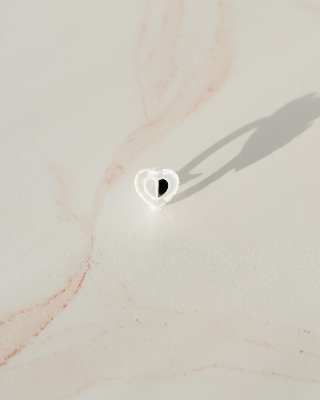 Beutimi Brave Hearts Ring in white heart shape with black center displayed on neutral beige marble surface