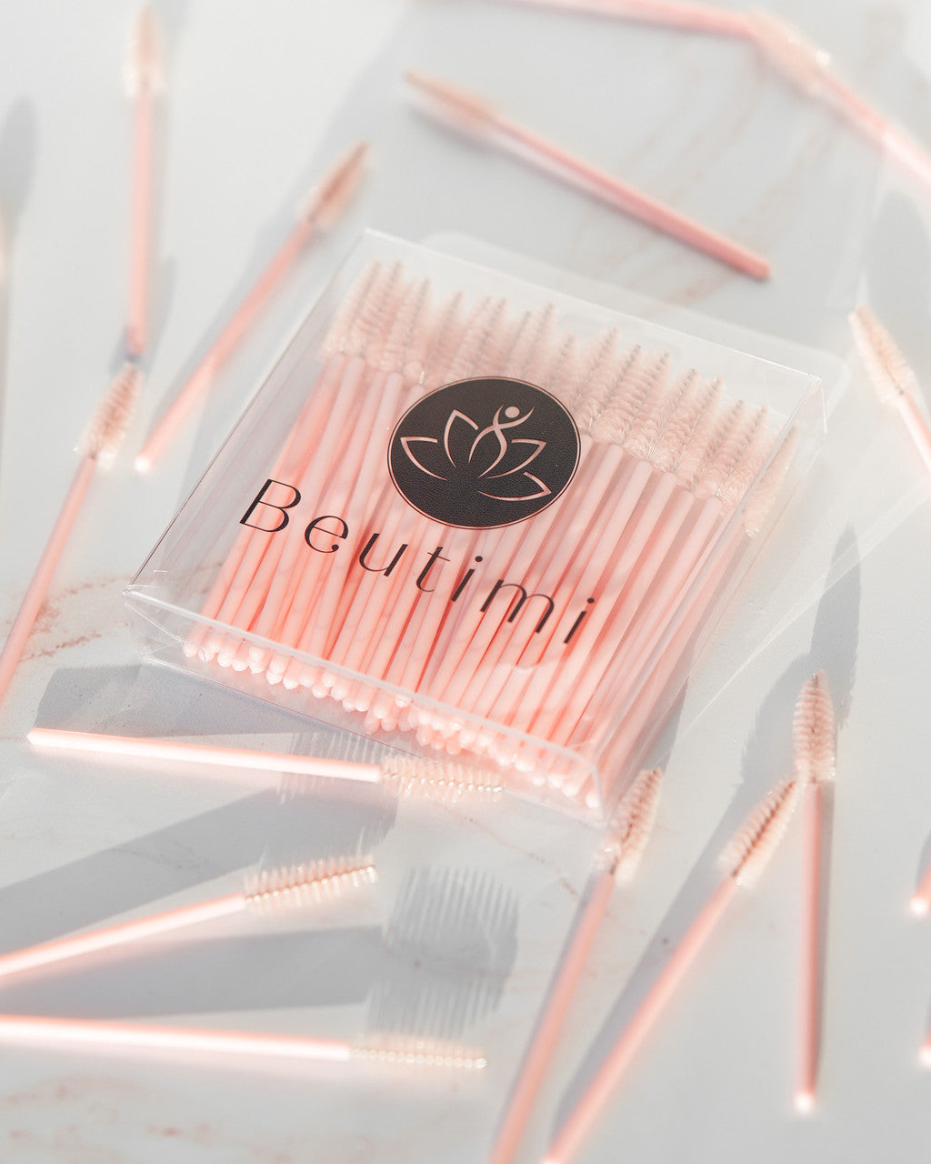 Beutimi Uplift Lash Spoolies in blush pink displayed in clear packaging with loose brushes scattered on white surface