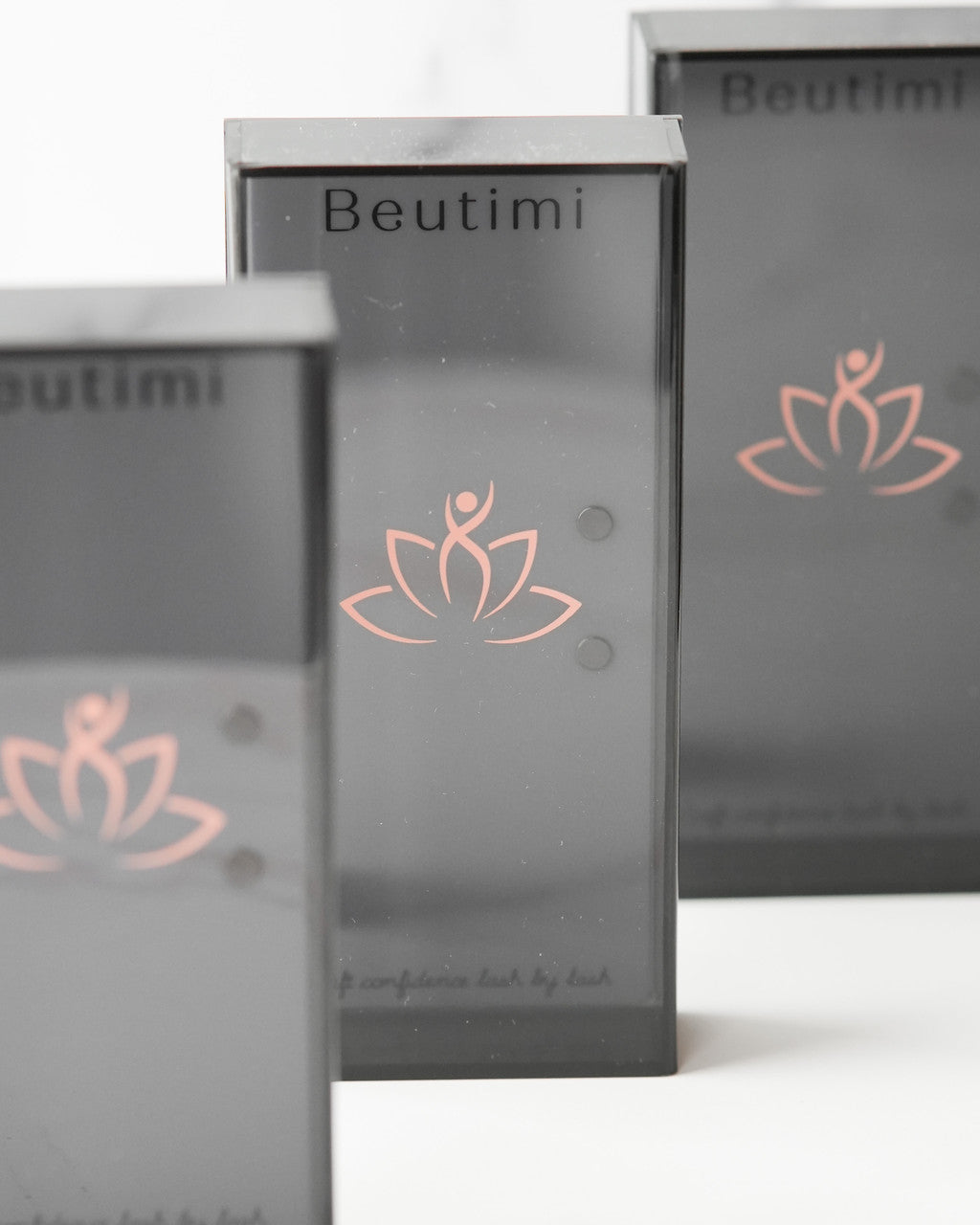 Beutimi Lash Visionary Tile boxes display matte gray packaging with coral lotus logo and magnetized tweezer holders