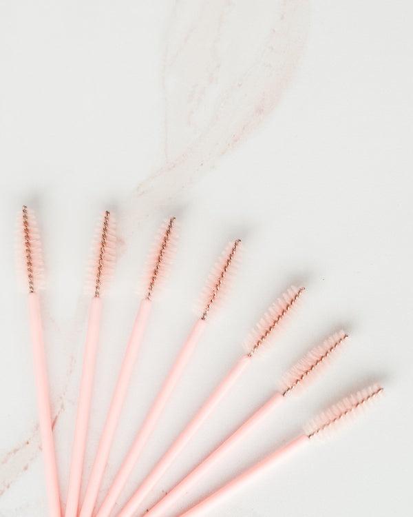 Seven blush pink Beutimi Uplift Lash Spoolies with rose gold bristles arranged on white marble background