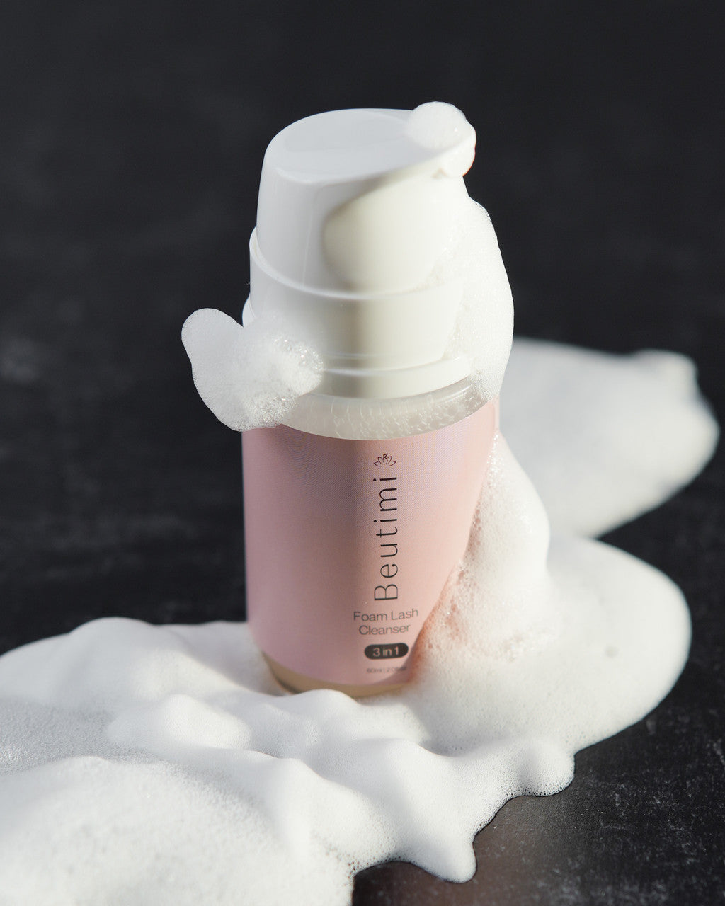 Beutimi Foam Lash Cleanser in pink bottle with white foaming lather overflowing against dark background