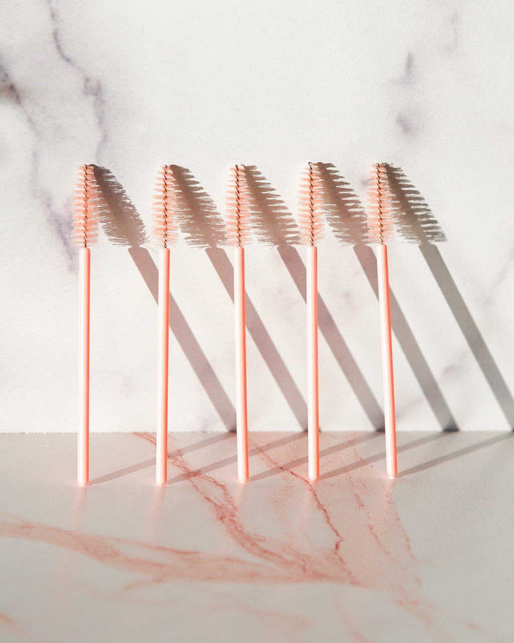 Five Beutimi Uplift Lash Spoolies with blush pink handles and soft bristle brushes arranged in a row on marble surface