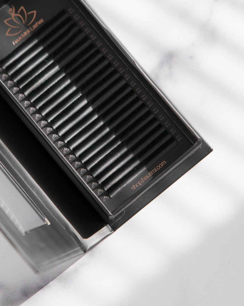Beutimi FauxMink Lashes 0.05MM arranged in black tray with organized lash strips and foil backing, overhead angled view