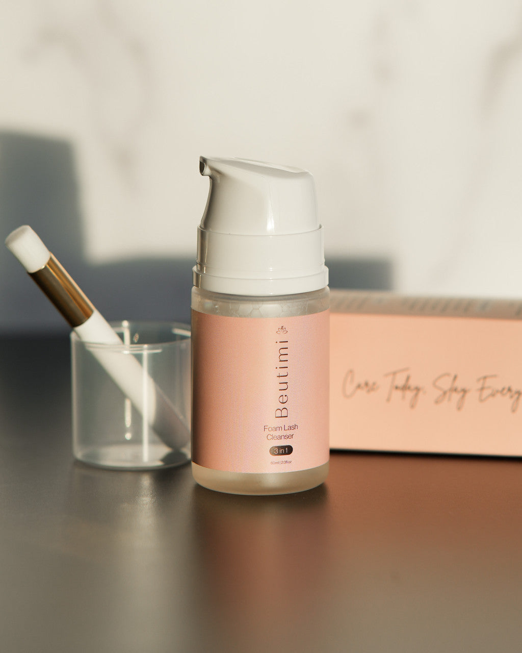 Beutimi Foam Lash Cleanser in peachy-pink pump bottle displayed with brush holder and branded packaging on neutral surface