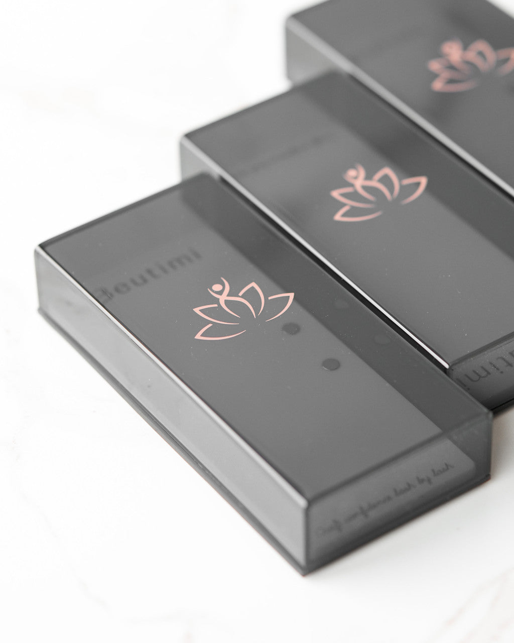 Three Beutimi Lash Visionary Tiles in gray with rose gold lotus logos arranged in a row on white background