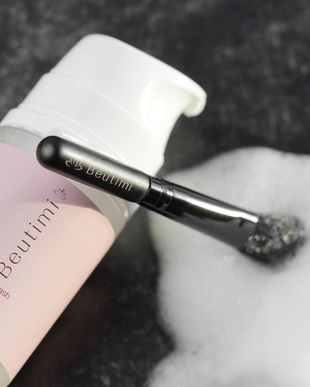 Beutimi Cleansing Brush with black handle and soft bristles displayed next to pink packaging on gray textured background