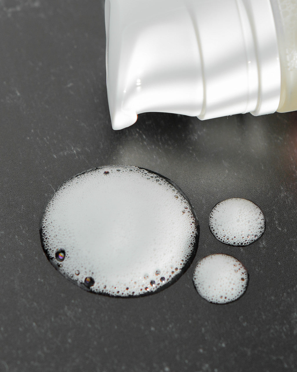 Beutimi Foam Lash Cleanser dispenses white foamy lather bubbles onto dark surface, showing rich texture and cleansing action
