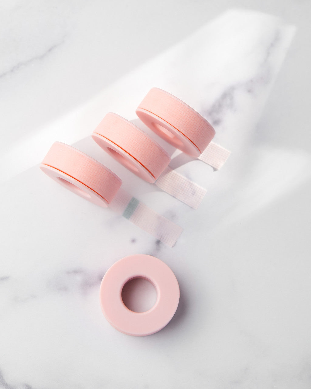 Beutimi Empower Gel Tape rolls in pink displayed on marble with one unwound spool showing the gentle adhesive tape