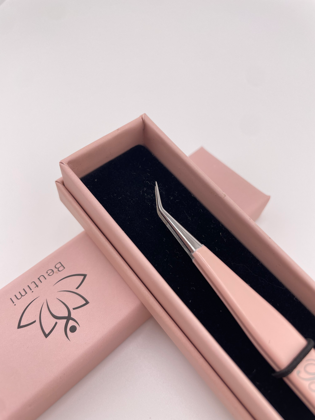 Beutimi Be Bold Tweezer with peach handle and curved fiber tip displayed in pink packaging with black velvet interior