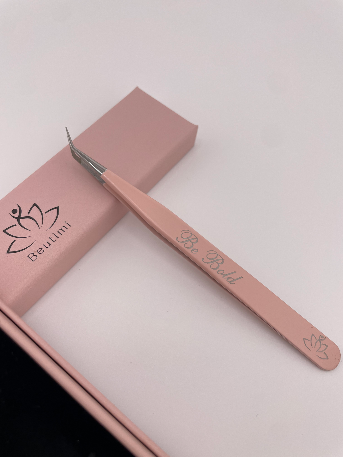 Beutimi Be Bold Tweezer in blush pink with curved fiber tip displayed next to its branded packaging box on white background