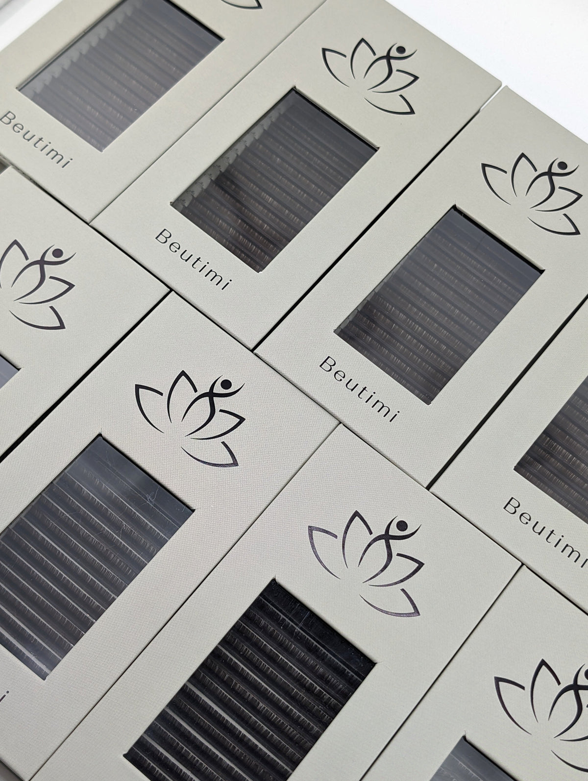 Beutimi Dark Brown FauxMink Lashes 0.05MM displayed in cream packaging with lotus logo and dark lash trays arranged diagonally