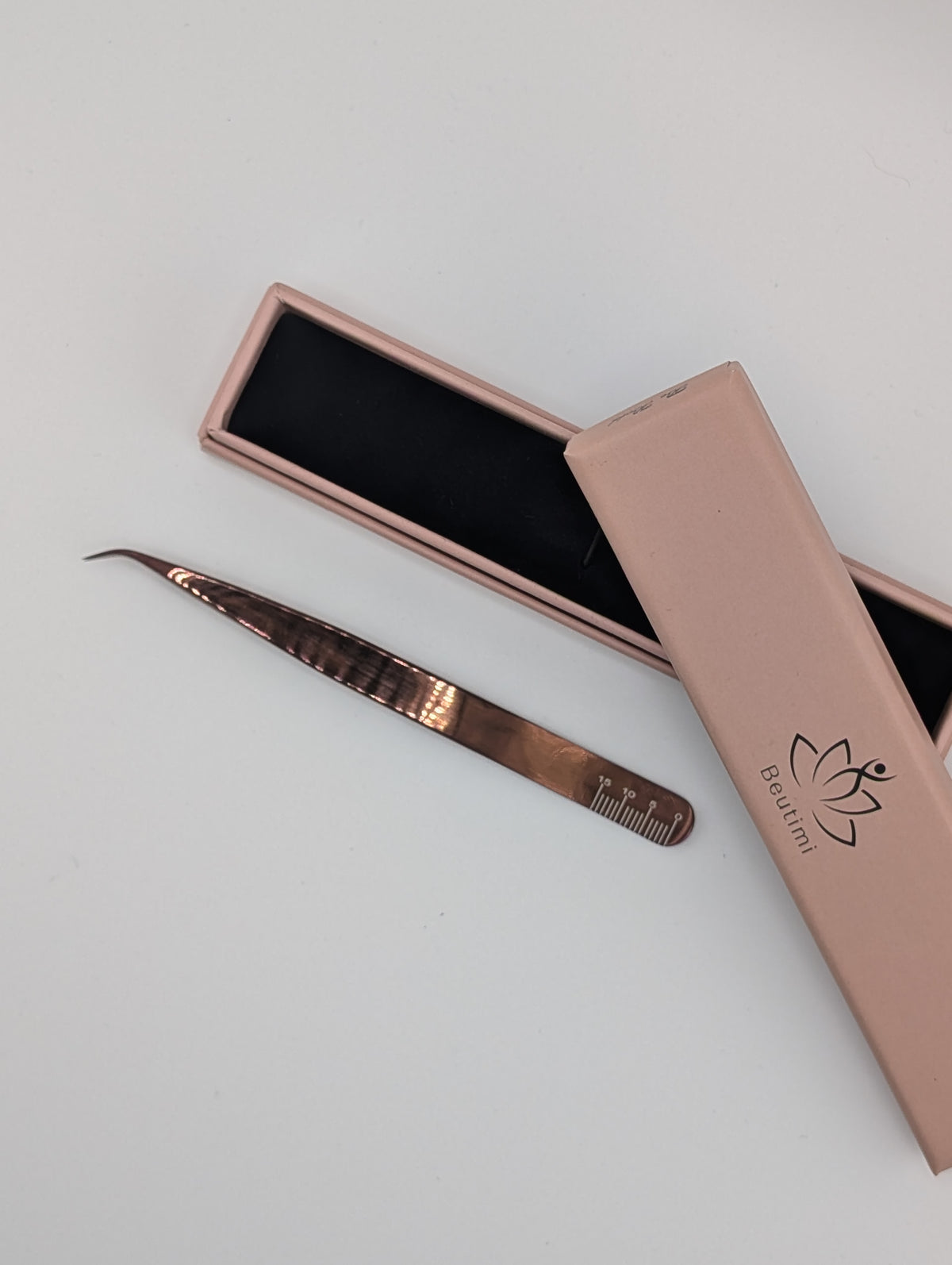 Beutimi Be Bold Tweezer in rose gold with curved fiber tip displayed next to its pink branded case with lotus logo