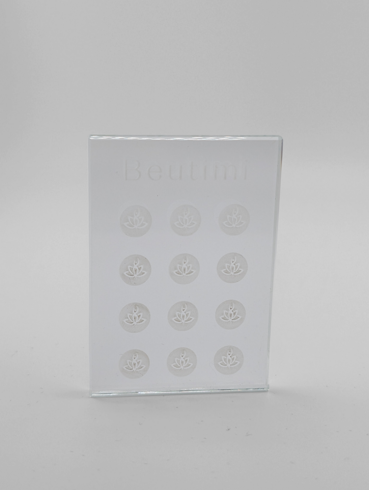 Beutimi Crystal Clear Adhesive Palette displayed as a frosted glass rectangle with twelve lotus-embossed circular wells arranged in rows