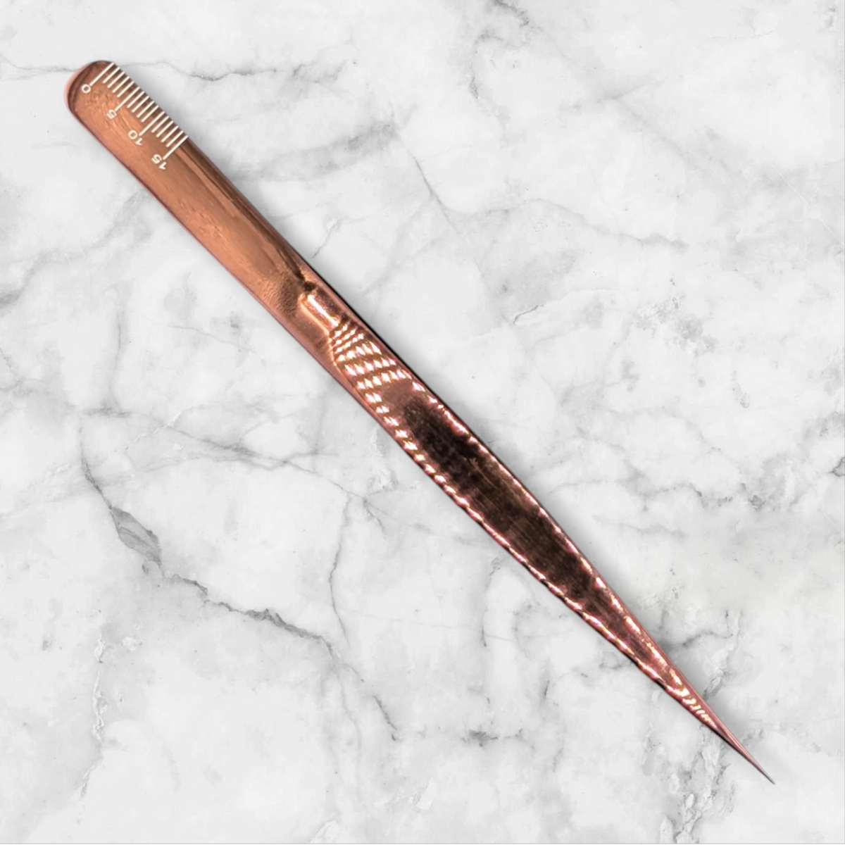 Beutimi On Point Tweezer in rose gold with fine-tooth comb head displayed diagonally on marble surface