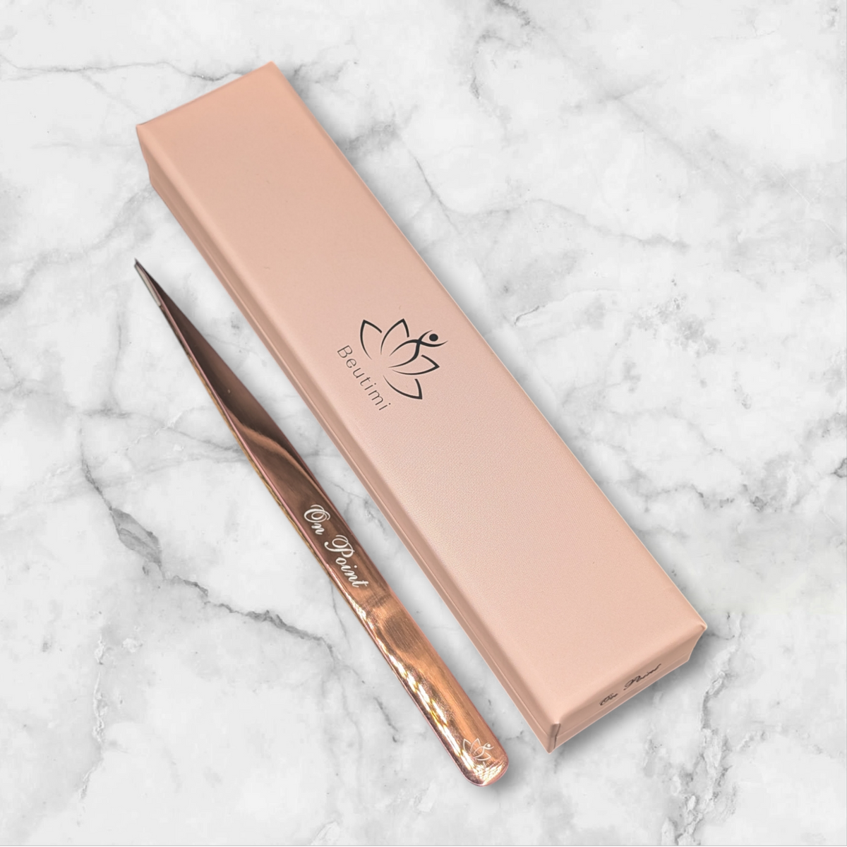 Beutimi On Point Tweezer with rose gold handle displayed next to its peachy-pink packaging on marble background
