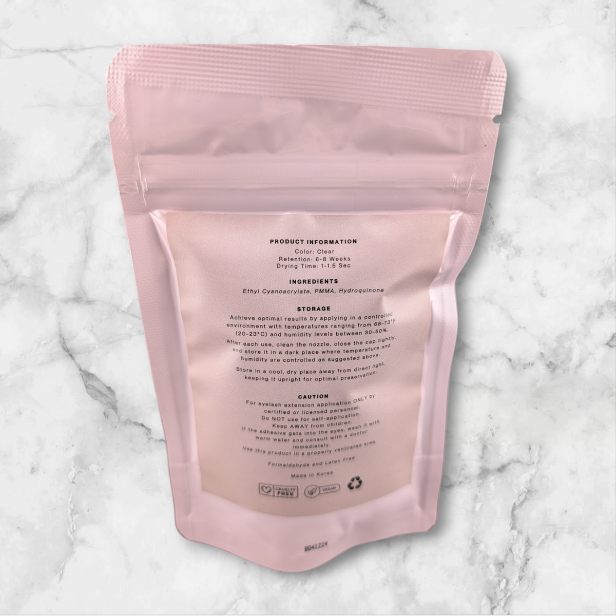Pink pouch of Beutimi Essence Clear Adhesive displayed flat against marble background showing product information label