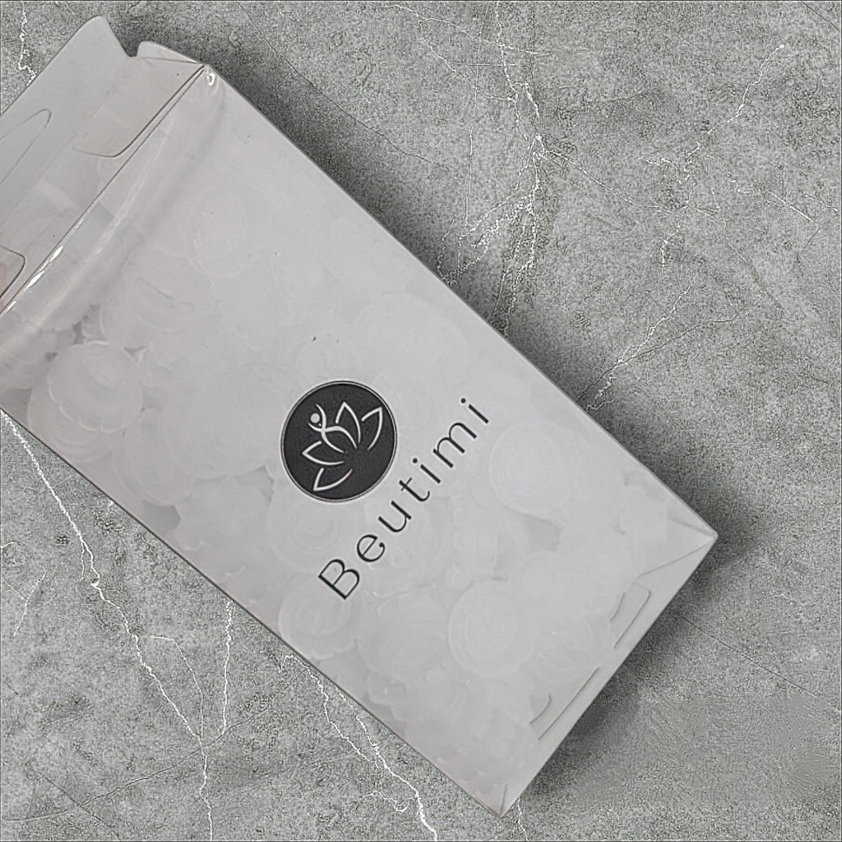 Beutimi Lotus Bouquet Ring package in white with black lotus logo displayed at an angle on gray concrete background